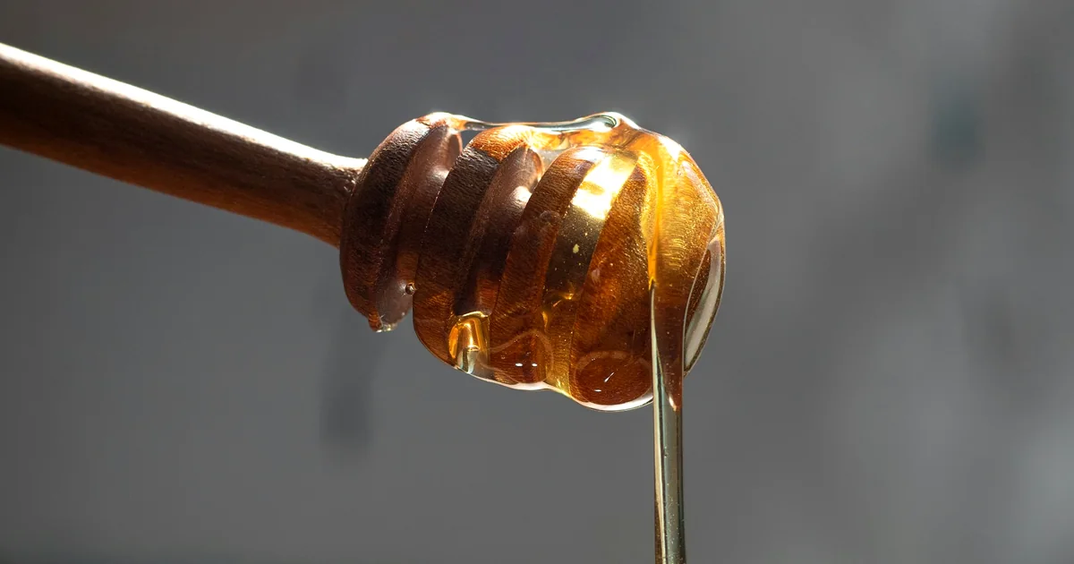 Miel doré coulant d'une louche en bois dans un bol brun